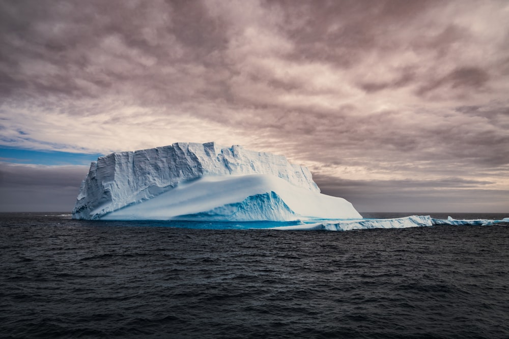 a large iceberg floating in the ocean under a cloudy sky