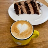 A slice of chocolate cake paired with a frothy cappuccino on a ceramic plate.