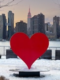 a large red heart sculpture in front of a city skyline