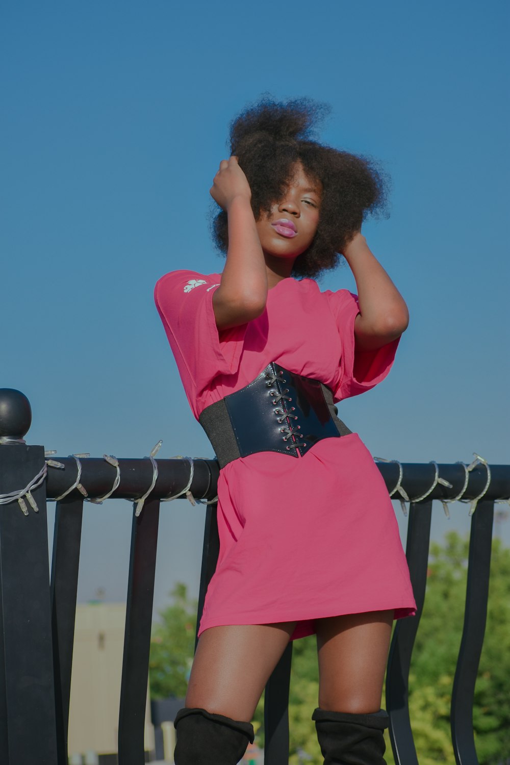 a woman in a pink dress leaning on a fence