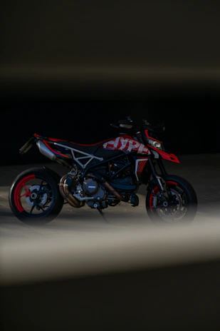 A sleek display of various motorcycle lubricant bottles arranged by viscosity and type, with a blurred background of a red sports motorcycle.