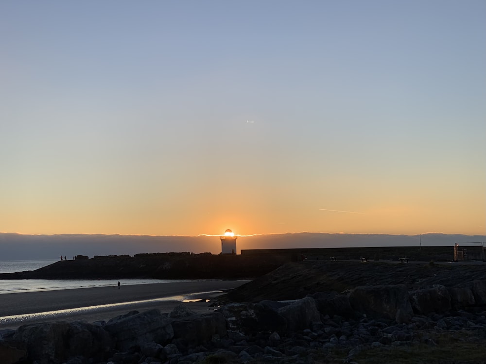 the sun is setting over the ocean with a lighthouse in the distance