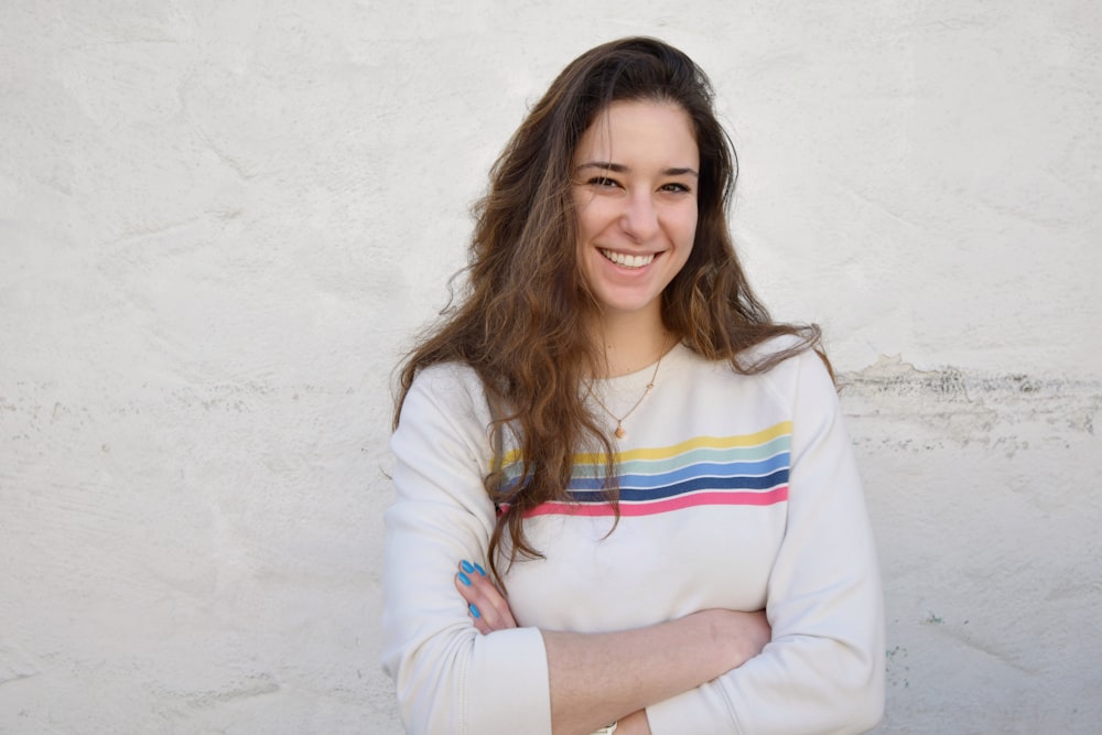 a woman standing with her arms crossed in front of a white wall