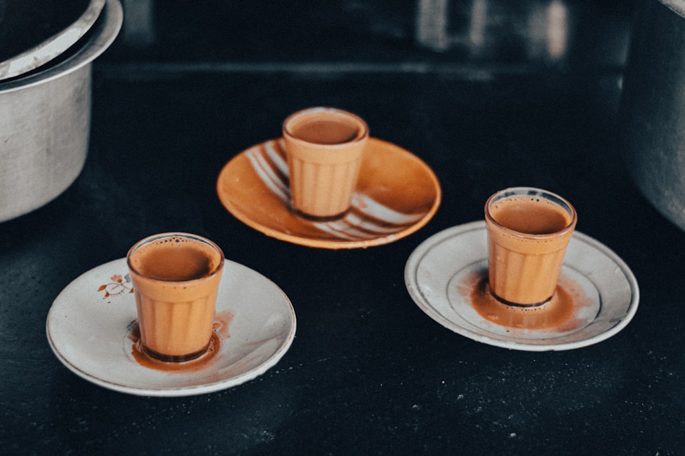 three orange cups and saucers on a black table