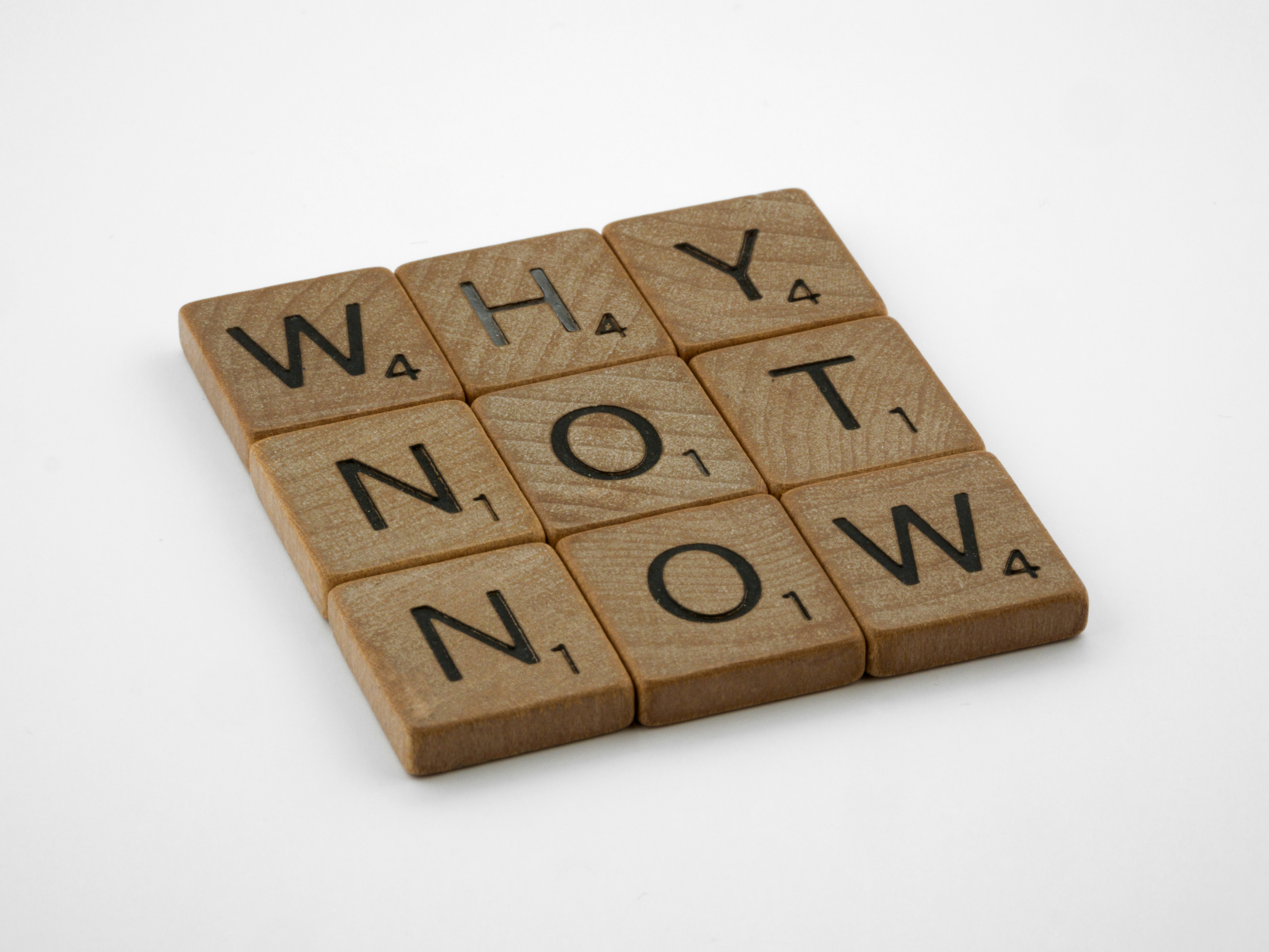 a scrabbled wooden block that says why not now