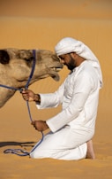 a man in a white outfit is petting a camel