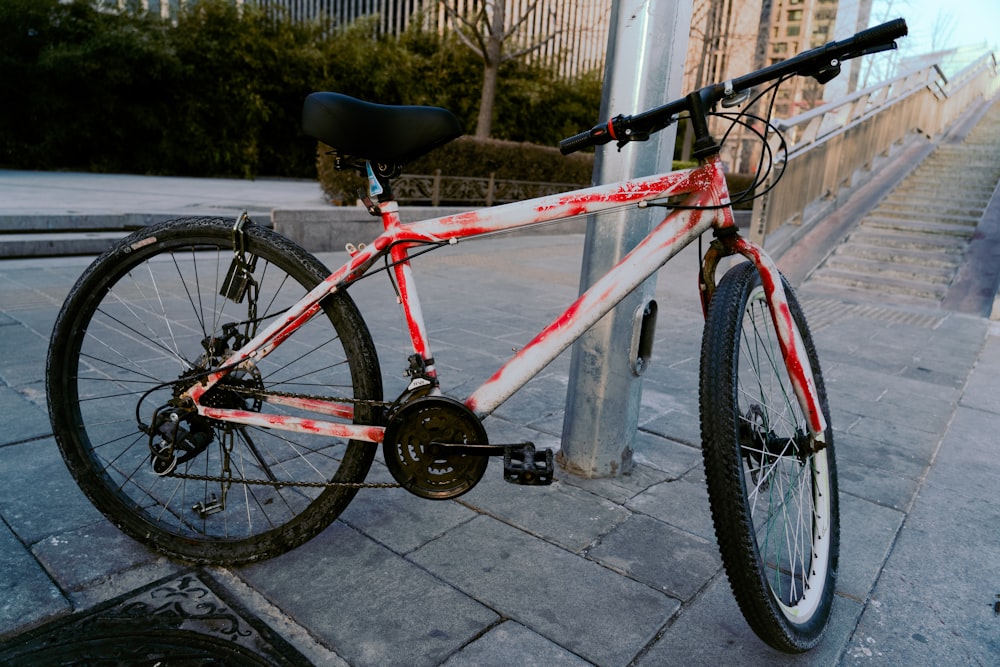 a red and white bicycle parked next to a pole