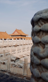 Historic Chinese architecture with ornate carvings and traditional orange-tiled roofs. The stone railings are intricately detailed, and a larger stone structure is prominent in the foreground.