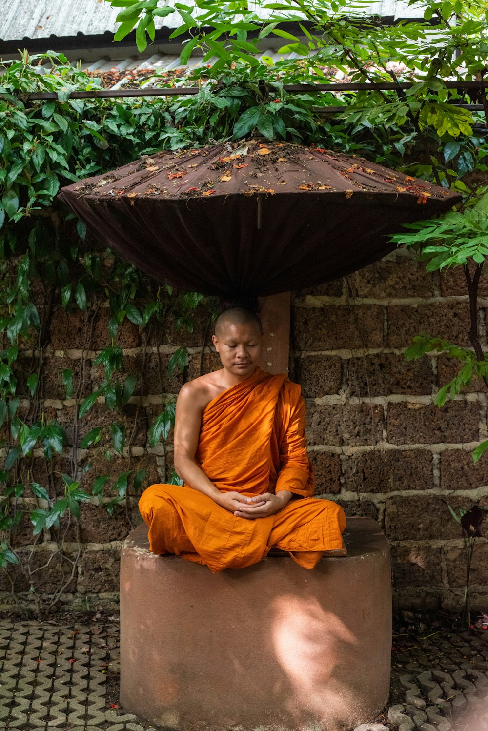 a monk sitting on a stone bench under an umbrella