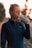 A person with a tied-back hairstyle is wearing a dark athletic jacket and drinking from a white reusable water bottle. The background is softly blurred with warm tones, suggesting a sunset or sunrise setting.
