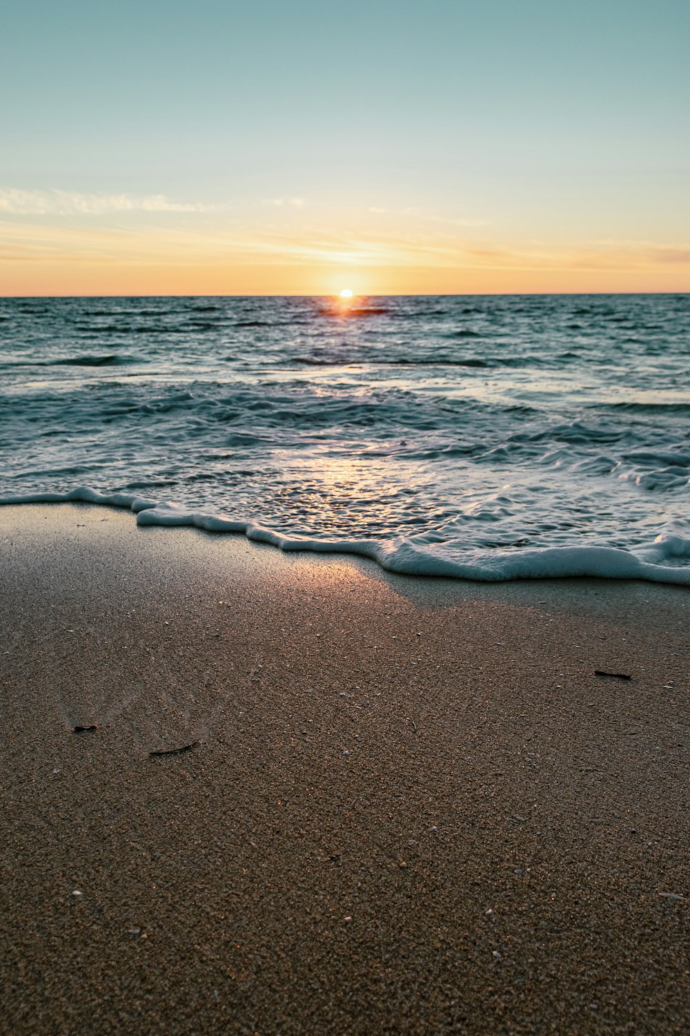 the sun is setting over the ocean on the beach