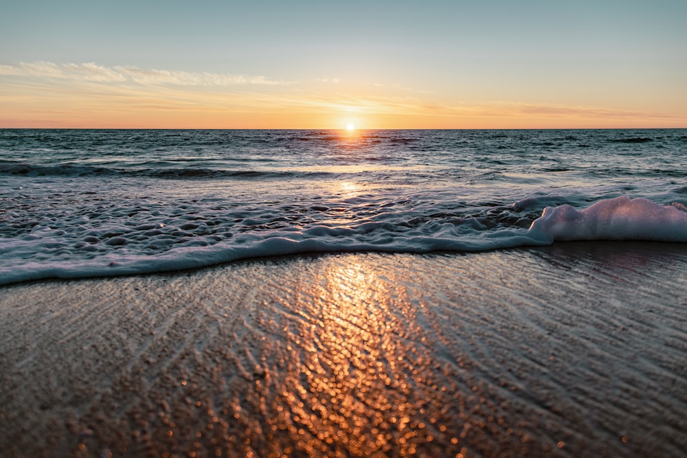 the sun is setting over the ocean on the beach