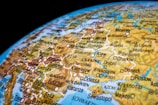 A detailed close-up of a colorful world globe featuring a focus on Eastern Europe. Various country names and cities, such as Warsaw, Budapest, and Moscow, are prominently labeled along with roads and bodies of water. The map includes topographical features with different shades for better differentiation.