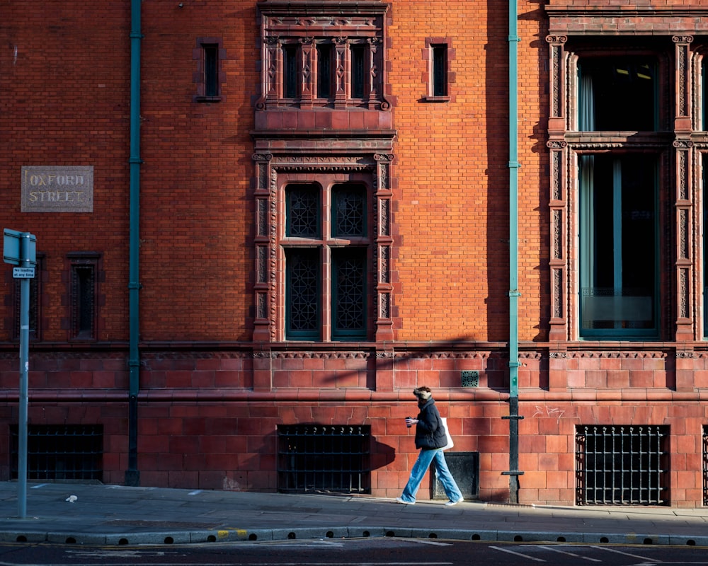 a man walking down a street past a tall brick building