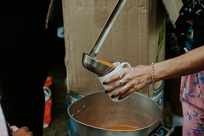 A volunteer pouring food into a serving pot at a charity meal program