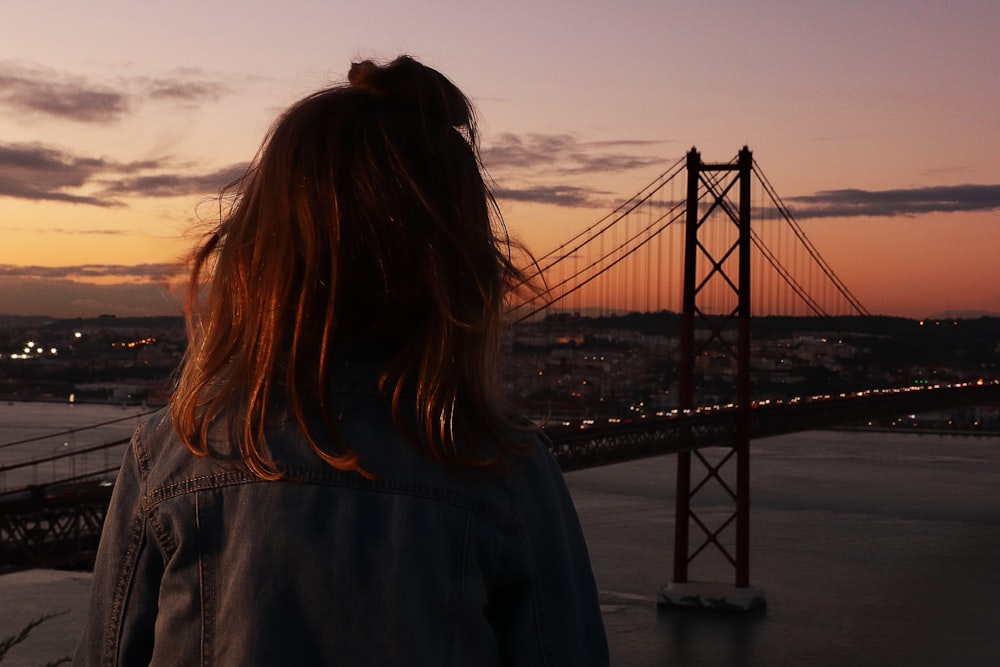 a woman standing in front of a bridge at sunset