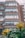 A multi-story brick building with large windows, labeled 'School of Education', is framed by green foliage and yellow flowers in the foreground. The building features modern architectural lines with a series of stacked, protruding window sections.