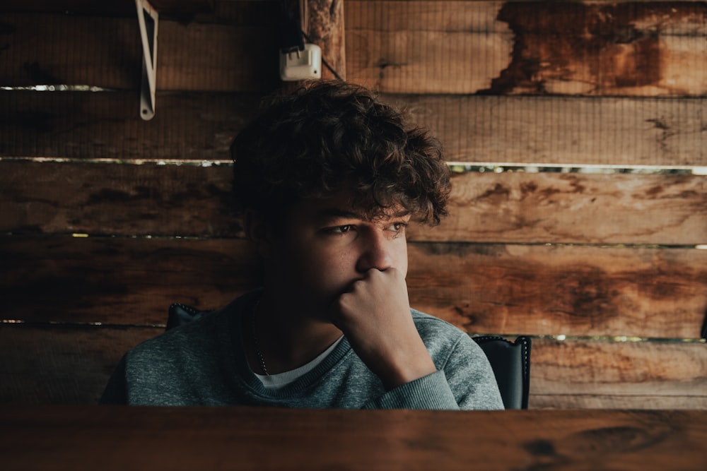 a young man sitting in front of a wooden wall