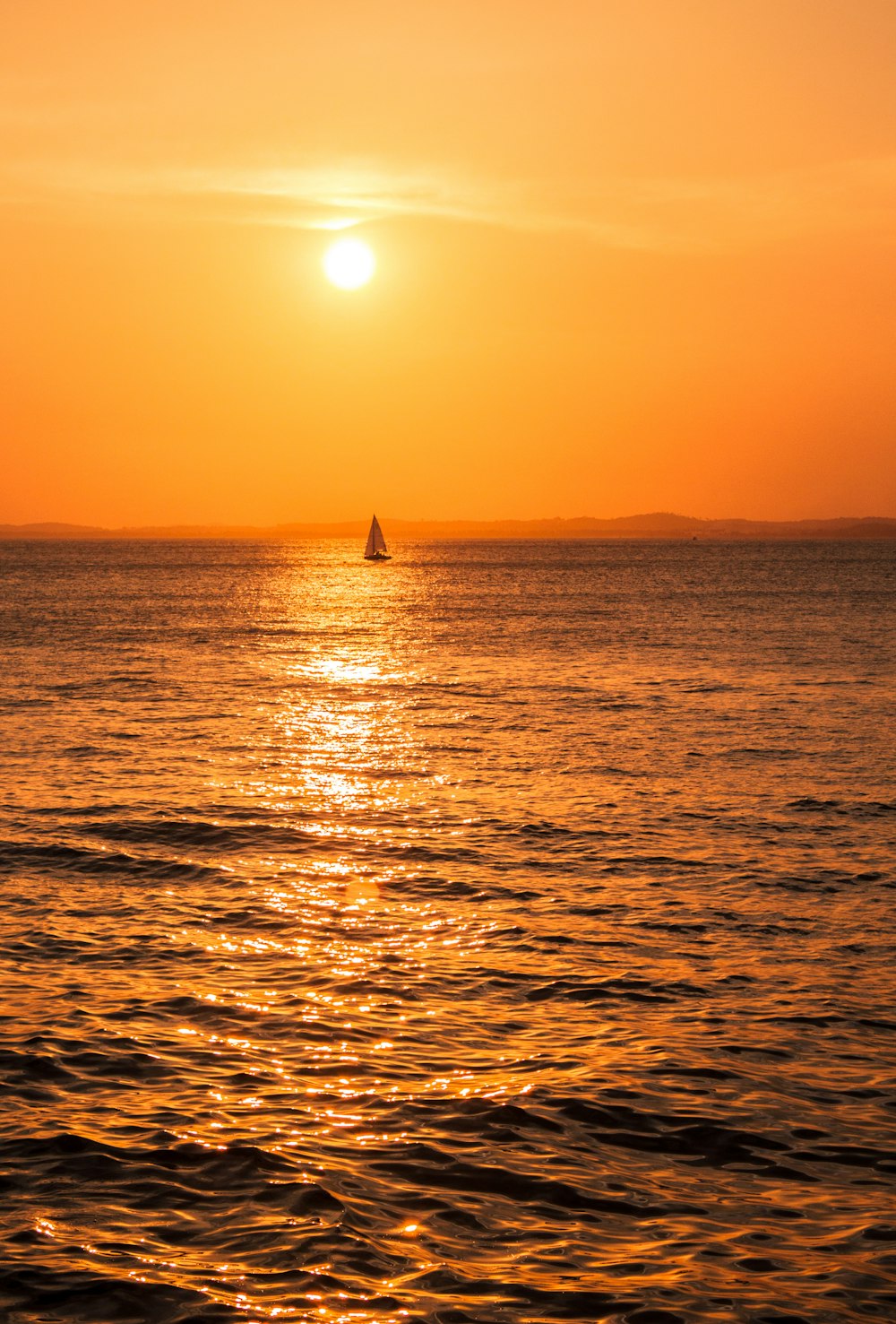 Il sole sta tramontando sull'oceano con una barca a vela in lontananza