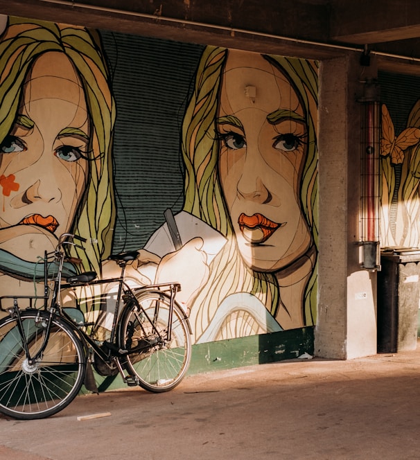 a bike parked next to a wall with a painting on it