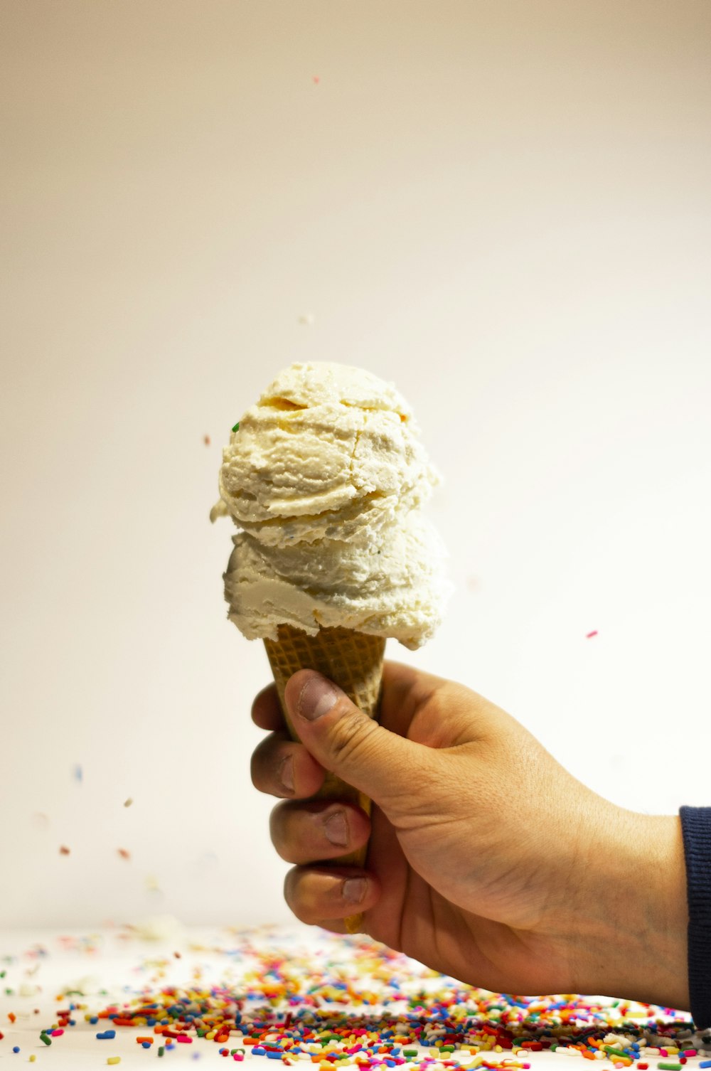 a hand holding an ice cream cone with sprinkles