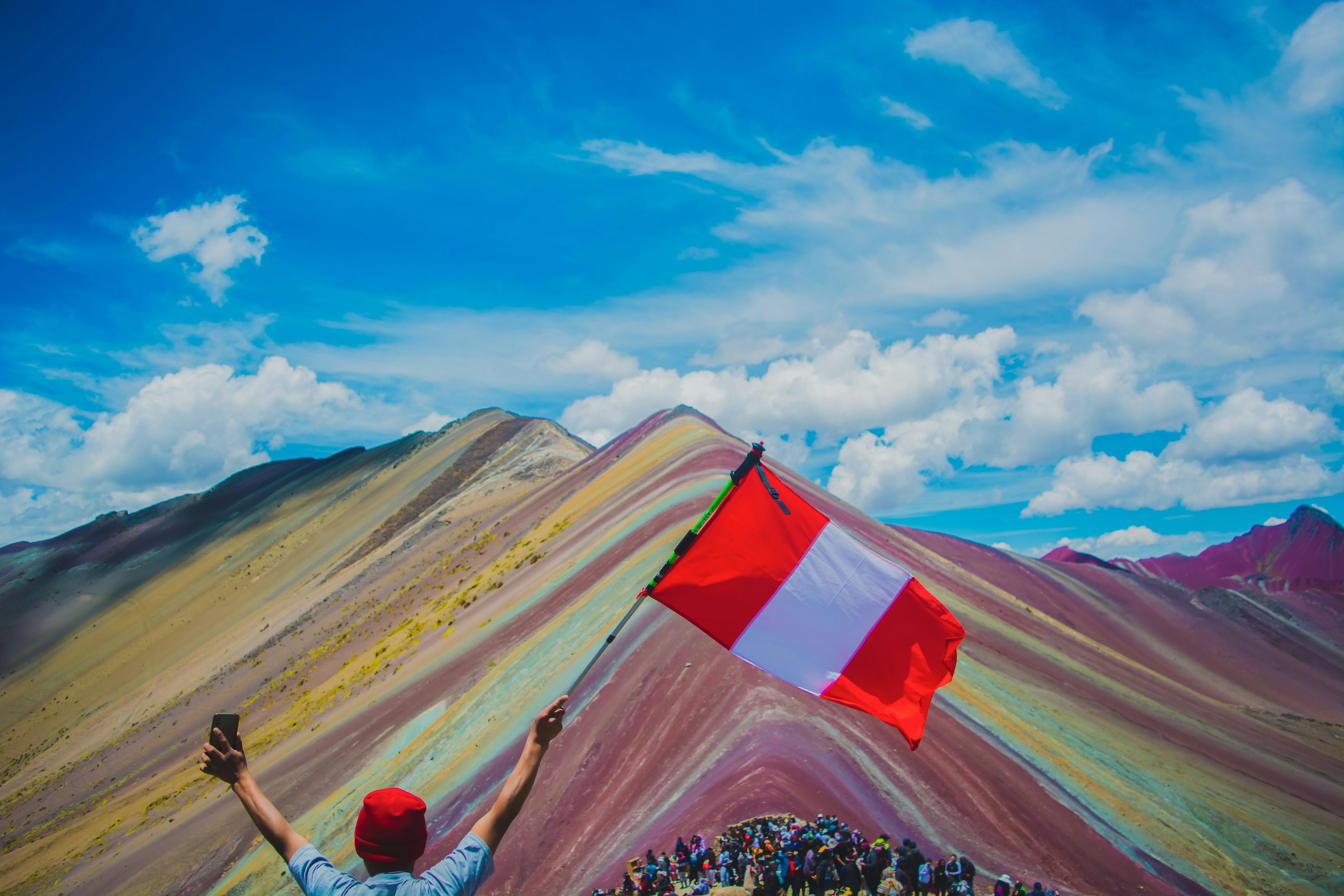 A man holding a flag on top of a mountain photo – Free Rainbow mountain ...