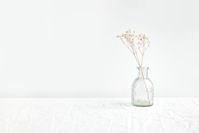 Close-up of a handcrafted plaster vase with delicate dried flowers inside, placed on a wooden table.