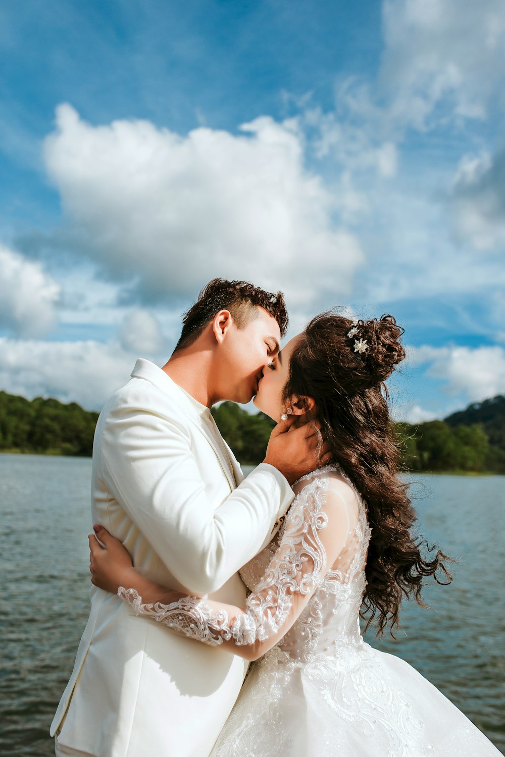 a bride and groom kissing in front of a lake