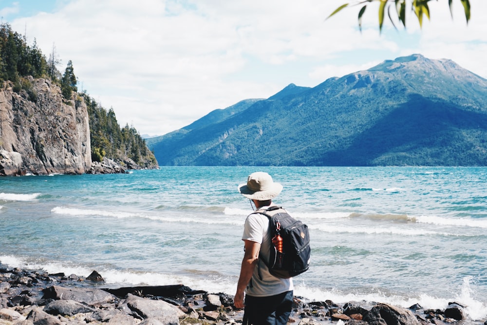 a man with a backpack standing on the shore of a lake