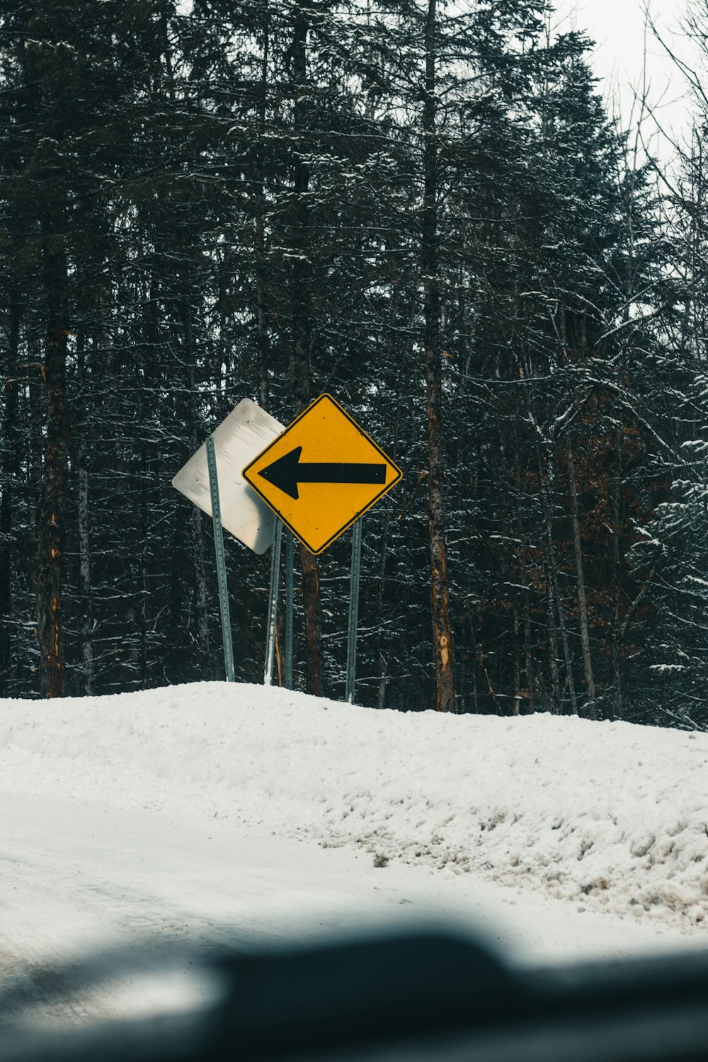 a yellow and white street sign sitting on the side of a snow covered road