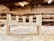 A partially assembled wooden furniture piece rests on a workshop table, surrounded by wood shavings. The background is a blurred view of a workshop, with shelves and tools visible.
