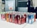 A collection of energy drink cans arranged on a white surface. The cans are from various brands, including Red Bull, Mountain Dew Kickstart, and Rise. They are organized in several rows, featuring a variety of colors and designs. The background is a blurred industrial setting.