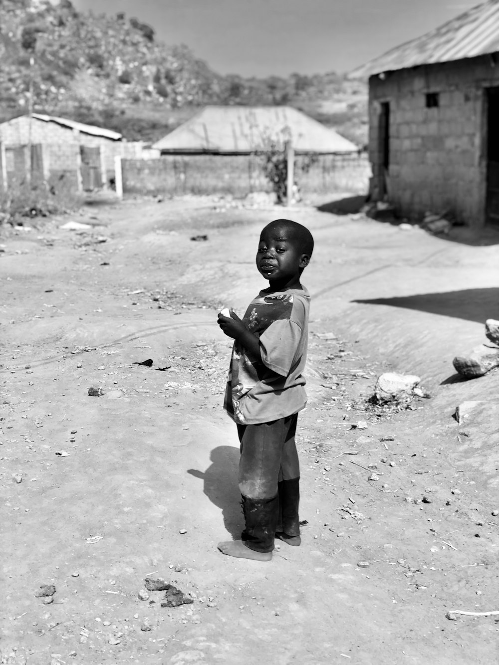 a little boy standing in the dirt near a building