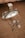 A silver-colored perfume bottle with a reflective surface is placed on a textured brown surface. Beside it, there is a pair of ornate, circular earrings with intricate detailing, as well as a matching pendant with a chain.
