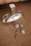 A silver-colored perfume bottle with a reflective surface is placed on a textured brown surface. Beside it, there is a pair of ornate, circular earrings with intricate detailing, as well as a matching pendant with a chain.