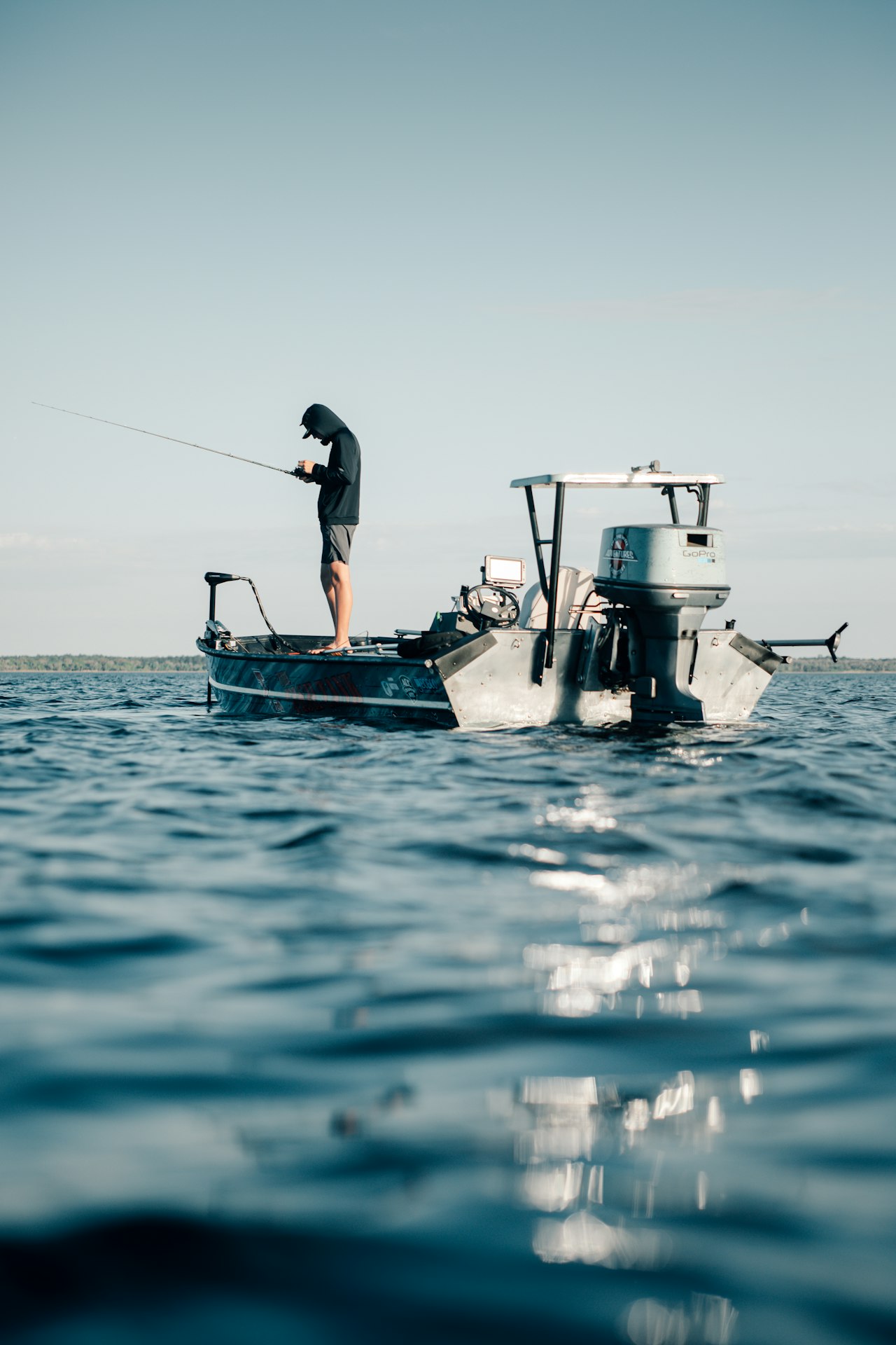 Angler checks a fishing rod aboard a small motorboat on open water.