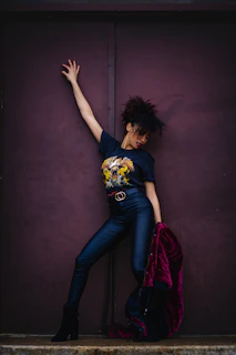 Model wearing a dark red t-shirt with a striking black graphic, standing in front of a black wall