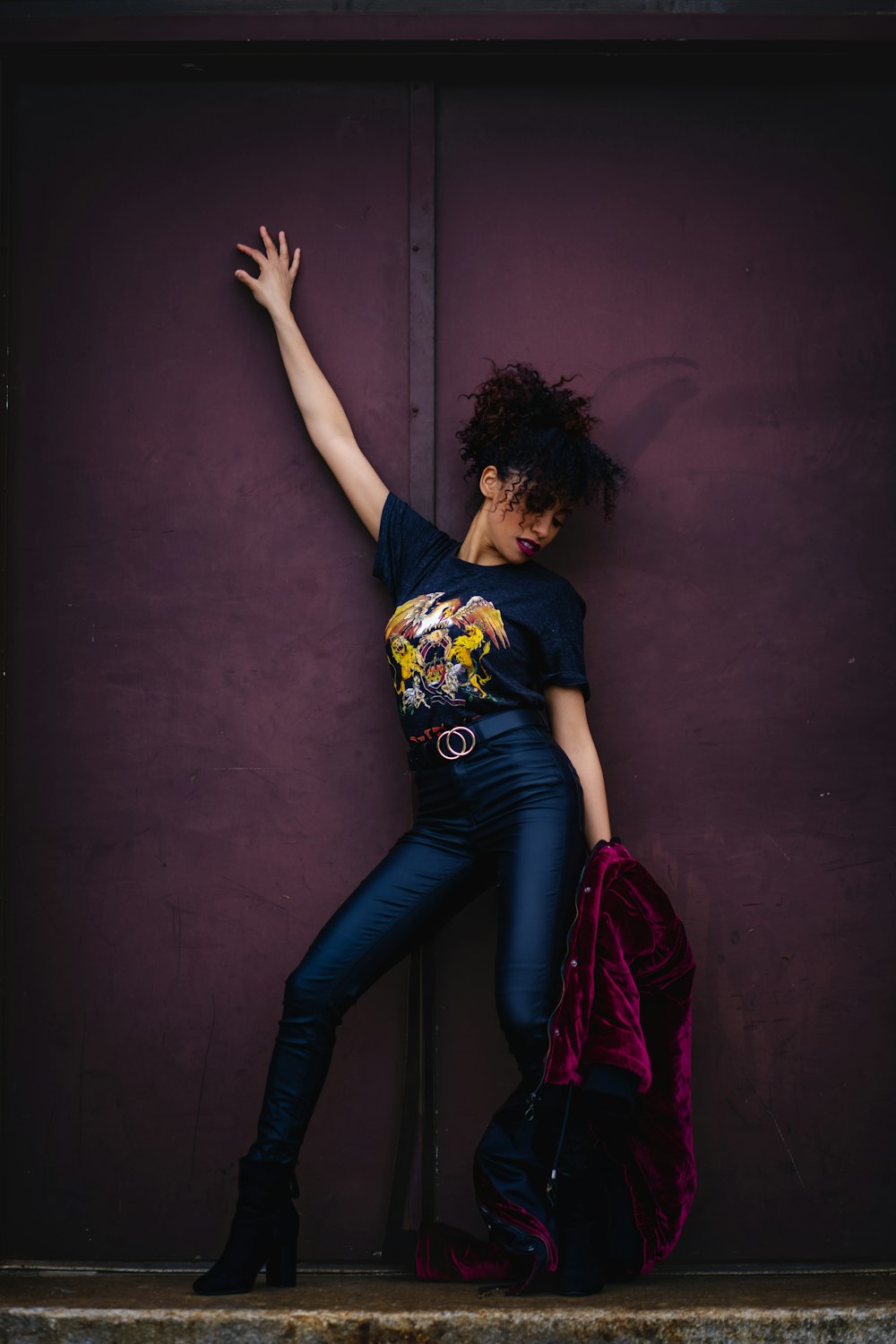 a woman leaning against a purple wall with her arms in the air