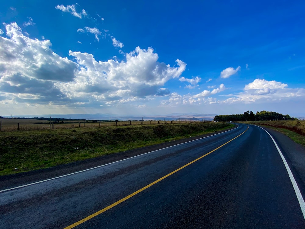 an empty road with a blue sky and white clouds