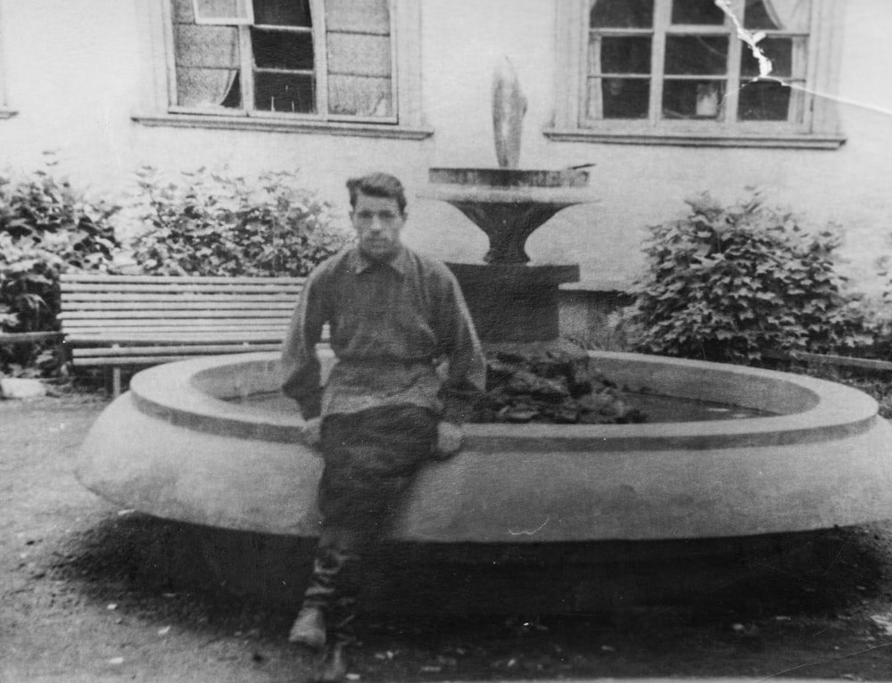 a black and white photo of a man sitting in front of a fountain