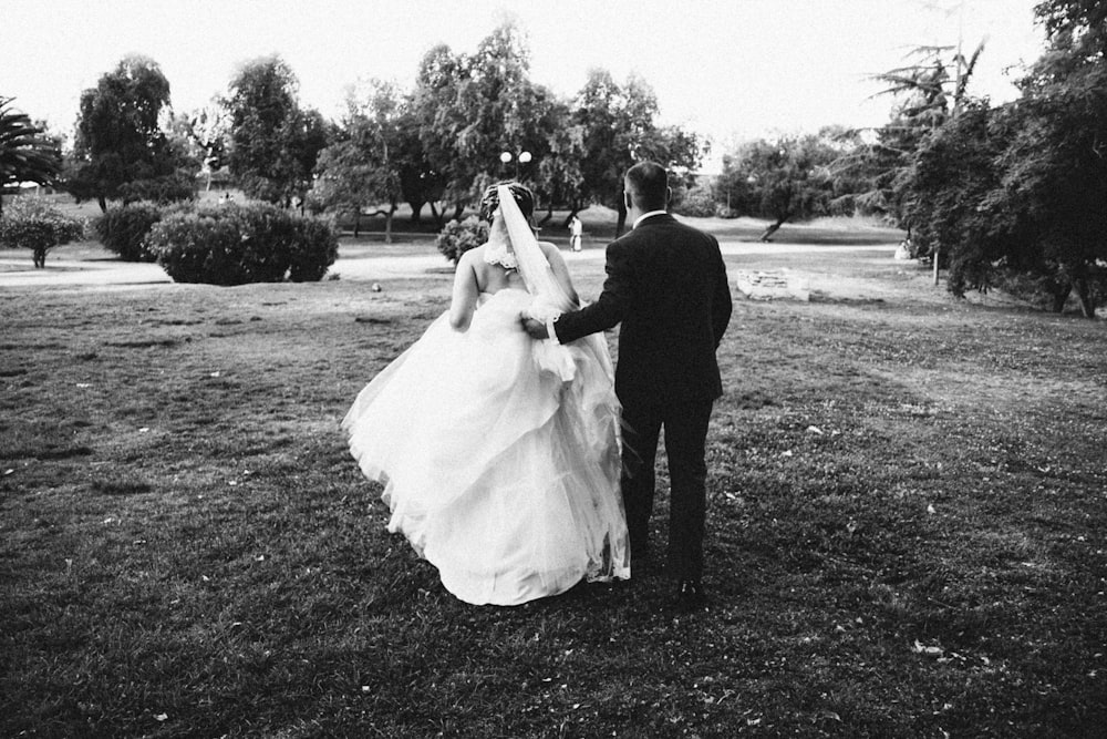 a bride and groom walking through a field