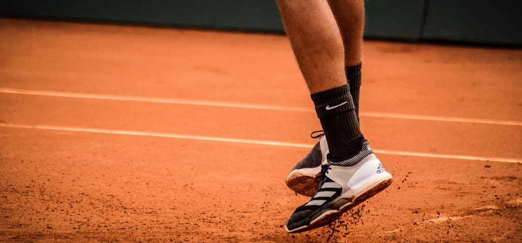 a tennis player's feet and shoes on a clay court