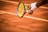 A close-up of a tennis player preparing to serve, holding a racket and a tennis ball. The court is clay, and the player's wristbands and racquet details are visible.