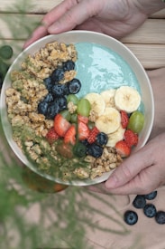 a person holding a bowl of fruit and cereal