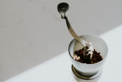 A sleek manual coffee grinder with freshly ground coffee spilling onto a rustic countertop.