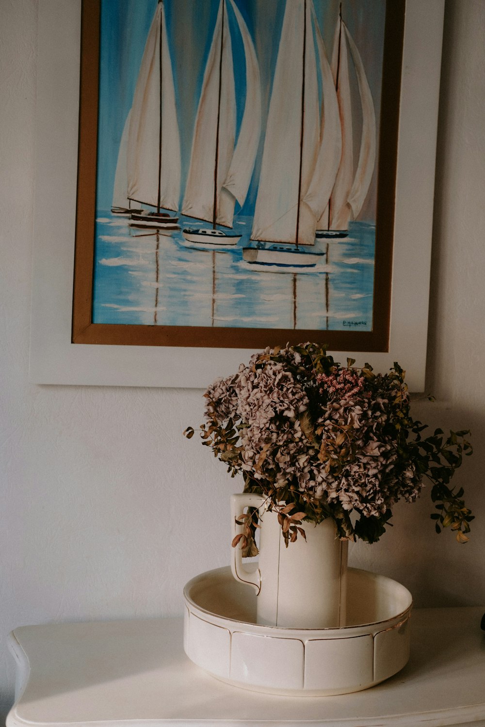 a painting of sailboats on a wall above a vase of flowers