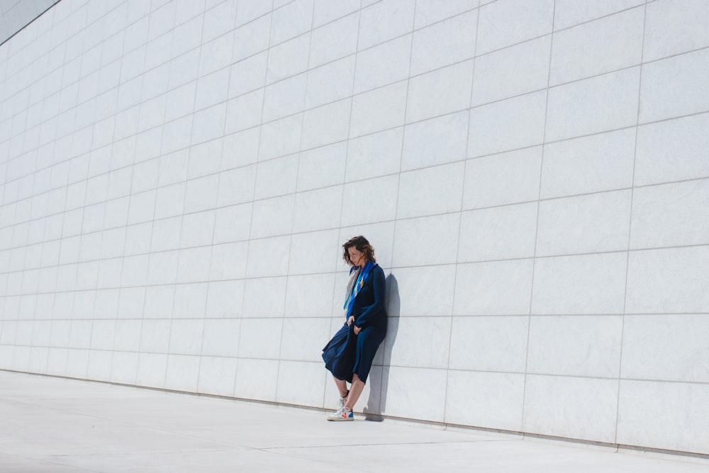 a woman leaning against a wall in a blue dress