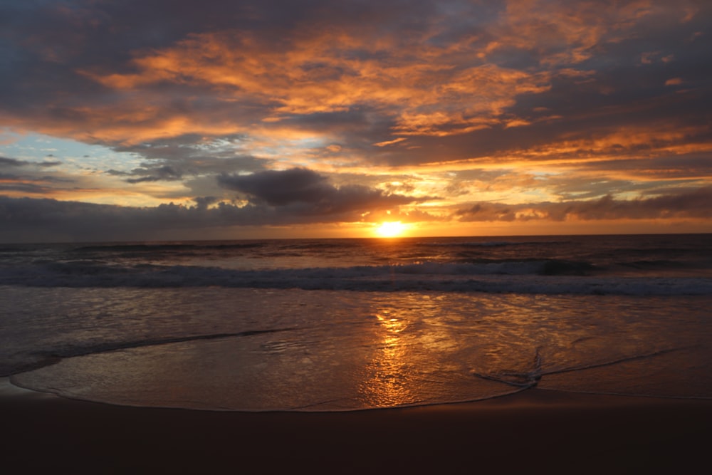 the sun is setting over the ocean on the beach