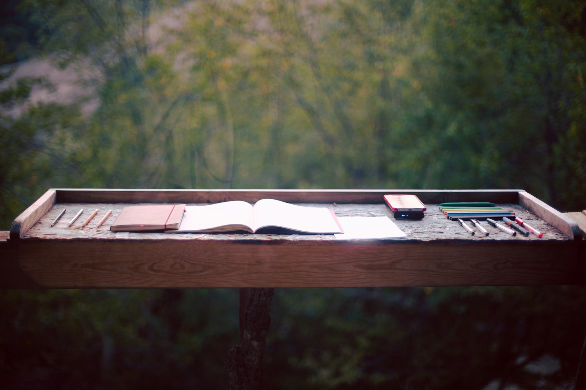 a desk with a book, pen, pencils, and other items on it