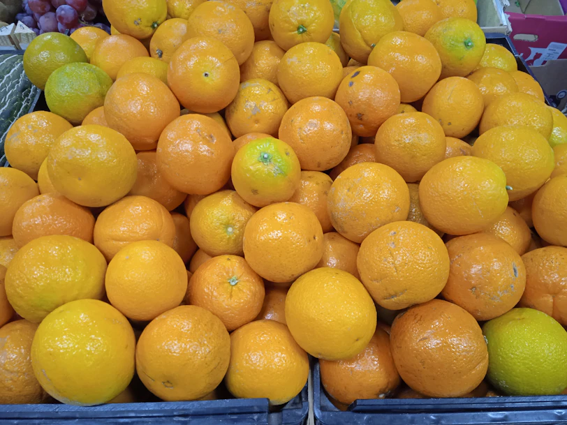 Fresh oranges and grapes displayed in a rustic wooden crate under natural sunlight
